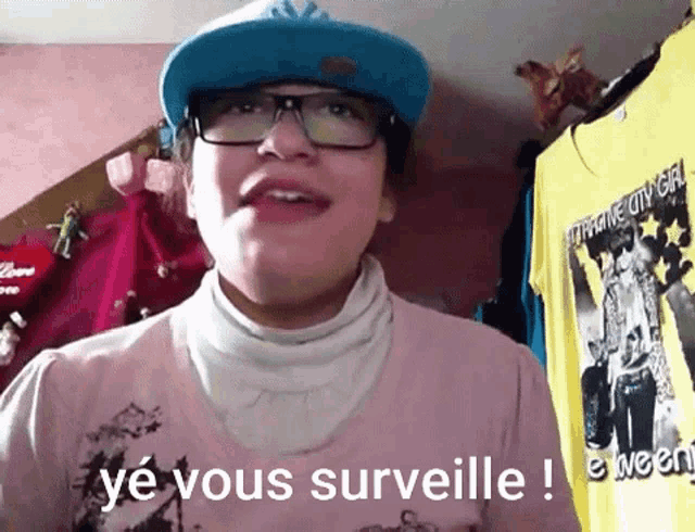 a person wearing glasses and a blue hat says ye vous surveille