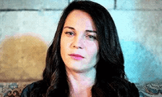 a woman with long dark hair is sitting on a couch and looking at the camera with a serious look on her face .