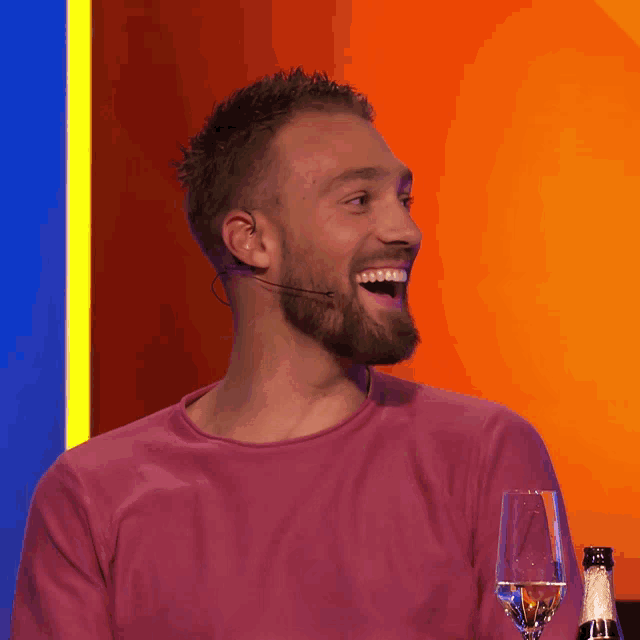 a man with a beard wearing a pink shirt and a microphone laughs