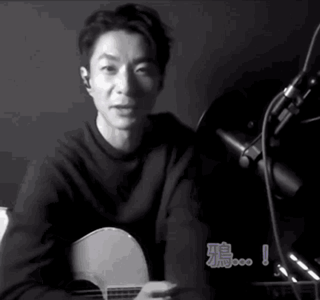 a man is playing a guitar in front of a microphone with chinese writing on it .