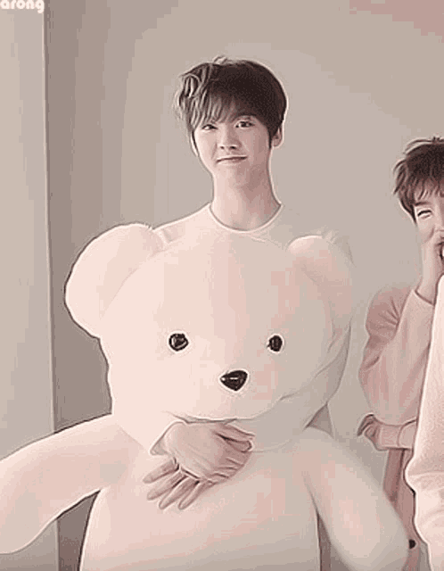 a young man holding a large white teddy bear with the word among written on the bottom