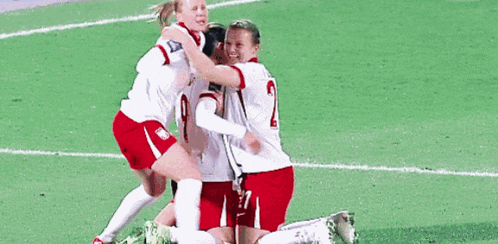 three female soccer players are hugging each other on the field .