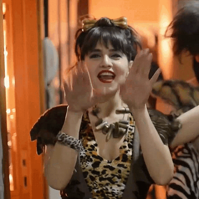 a woman wearing a leopard print top is waving her hands in the air