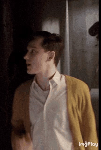 a man wearing a white shirt and a yellow cardigan is standing in a dark room .