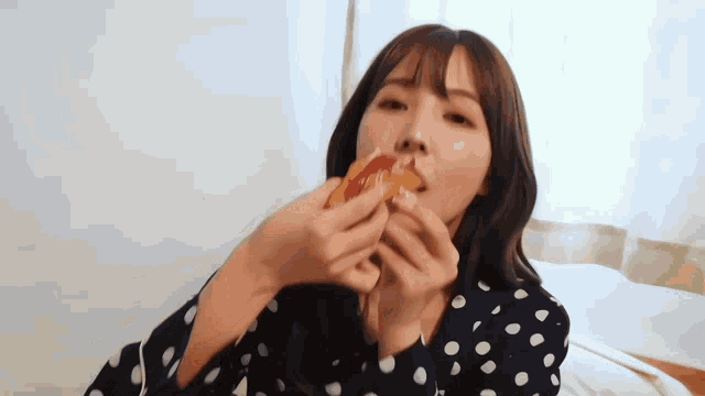a woman in a polka dot shirt is eating a slice of pizza