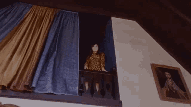 a woman is sitting on a balcony with a picture of a man on the wall behind her