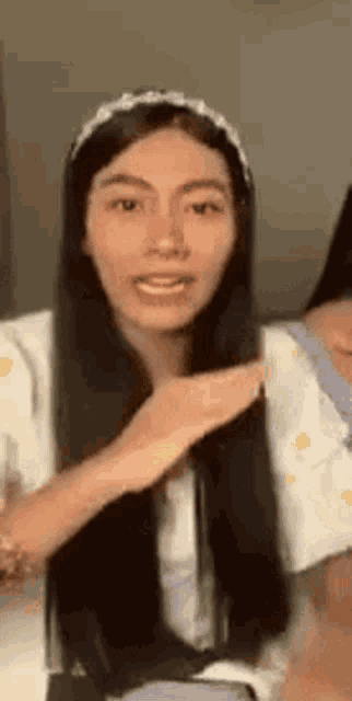a woman with long black hair is wearing a headband and a white shirt .