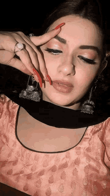 a woman with long red nails is wearing a pink top