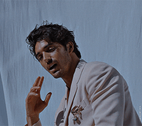 a man wearing a white jacket has his hands folded in front of his face