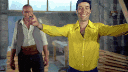 a man in a yellow shirt stands next to another man in a gray vest