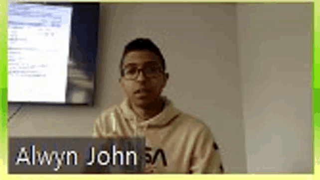 a man wearing glasses and a hoodie is standing in front of a tv .