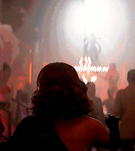 a woman in a red dress stands in front of a crowd in a dark room