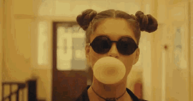 a woman wearing sunglasses is blowing a bubble with a bubble gum .