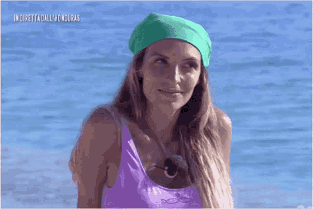 a woman wearing a purple tank top and a green headband is sitting on a beach .
