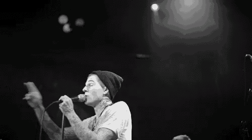 a man in a beanie is singing into a microphone on a stage in a black and white photo .