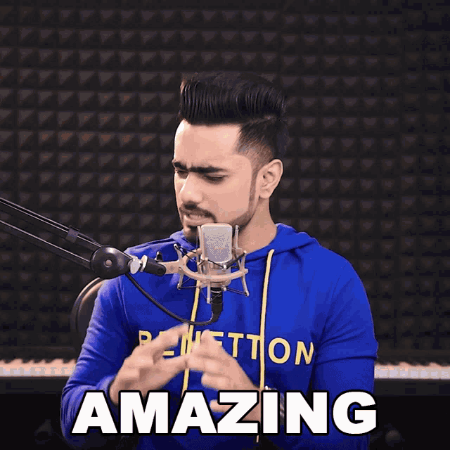 a man in a blue benetton sweatshirt sings into a microphone and says amazing