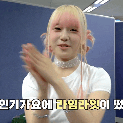 a girl with pink hair is clapping her hands in front of a sign that says ' korean ' on it