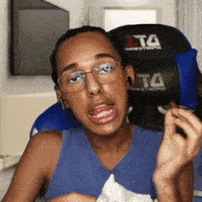 a man wearing glasses and a blue tank top is sitting in a chair with a t4 logo on it