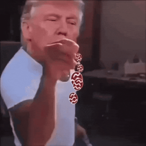 a man in a blue shirt is pointing at the camera while wearing a bracelet with red and white circles on it .