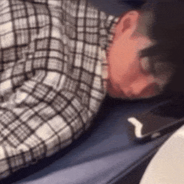 a man in a plaid shirt is sleeping on a bed next to a cell phone