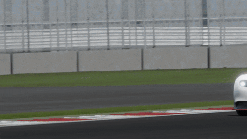 a white car is driving down a track with a red stripe on the side