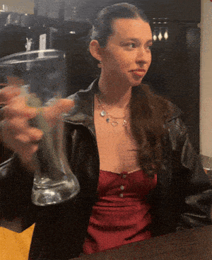 a woman in a leather jacket is holding a glass of water
