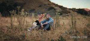 a man and woman are sitting in a field with a gifrun.com logo
