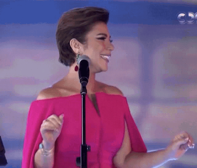 a woman in a pink off the shoulder dress sings into a microphone