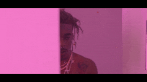 a man with dreadlocks is peeking out from behind a pink wall .