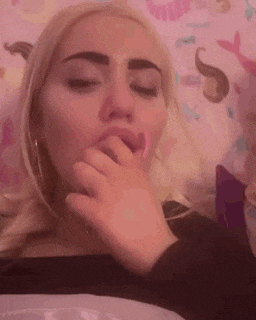 a woman with blonde hair is laying on a bed with her eyes closed and her hand in her mouth