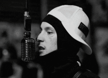 a man is singing into a microphone with a sticker on his hat that says bit