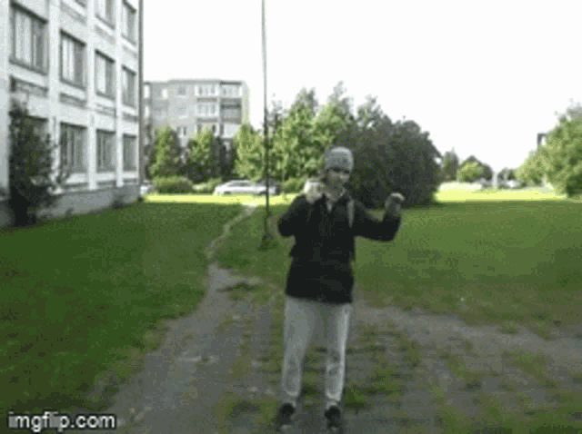a man in a black jacket is dancing in a park with imgflip.com on the bottom right