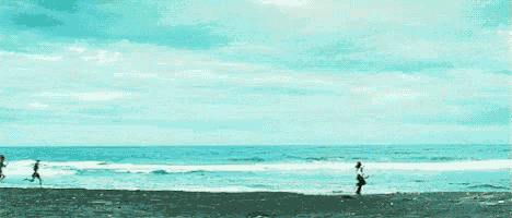 a group of people are running across a beach near the ocean .