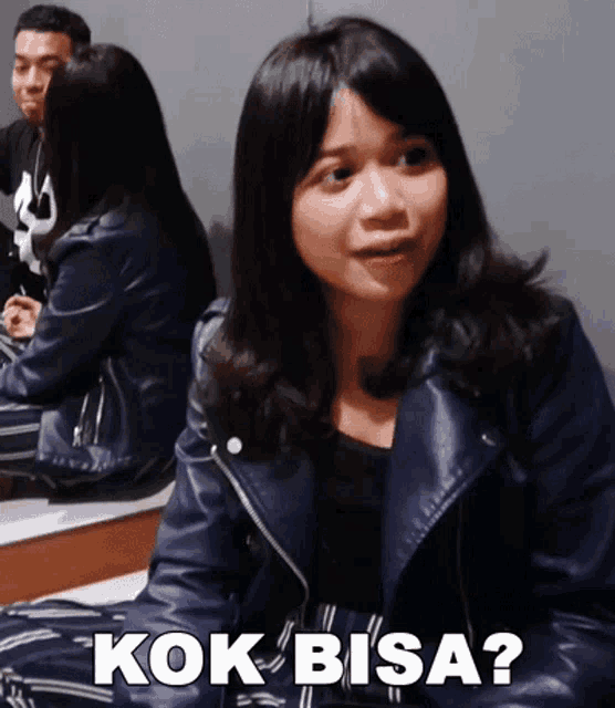 a woman in a leather jacket is sitting on a bench with the words kok bisa written below her