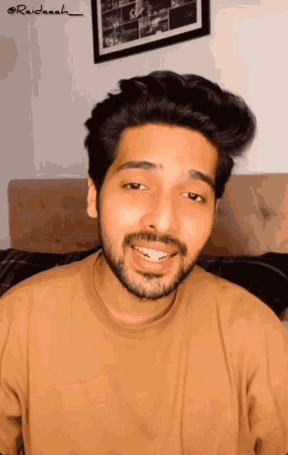 a man with a beard is smiling in front of a picture that says raidaash