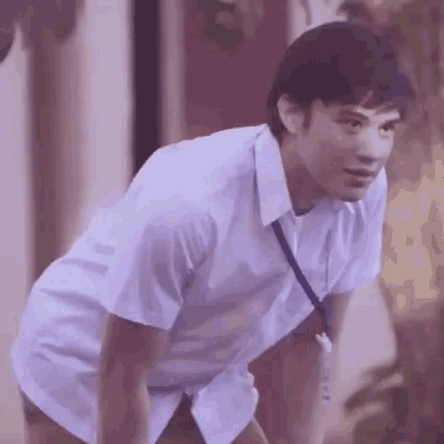 a young man in a white shirt is bending over and looking down .
