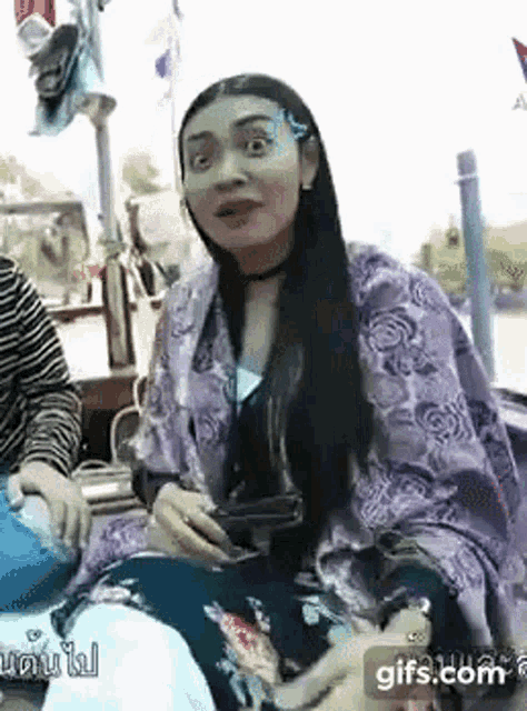 a woman with long black hair is wearing a purple scarf around her neck and holding a cell phone .