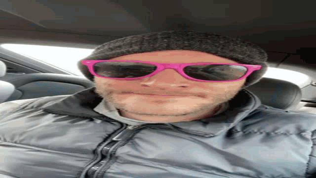 a man wearing sunglasses and a beanie is sitting in the back seat of a car