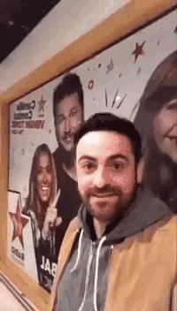 a man with a beard is taking a selfie in front of a large billboard .
