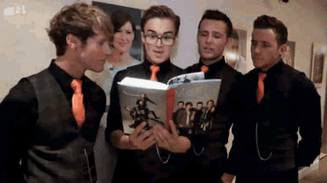 a group of men wearing black shirts and orange ties are reading a book together