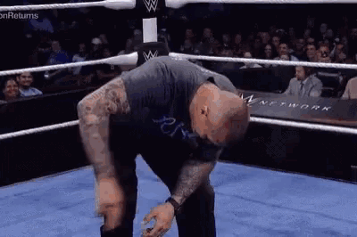 a man is bending over in a wrestling ring while a crowd watches .