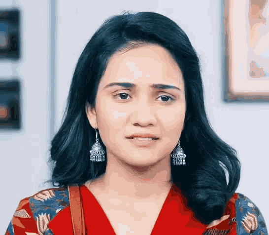 a woman wearing a red top and earrings looks at the camera