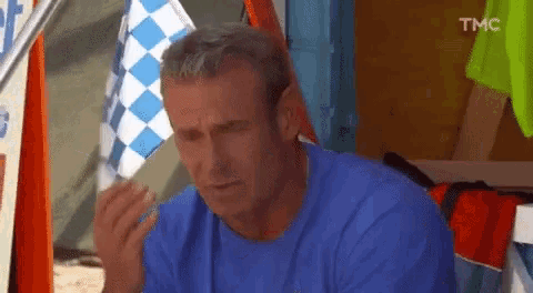 a man in a blue shirt is eating a sandwich in front of a sign that says tmc .