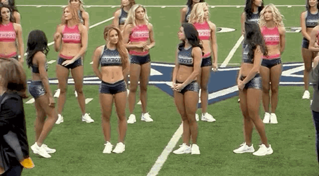 a group of cheerleaders are standing on a football field with a cowboys logo in the background .