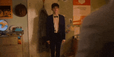 a man in a suit and bow tie stands in front of a wall with a poster that says bridesmaid visited