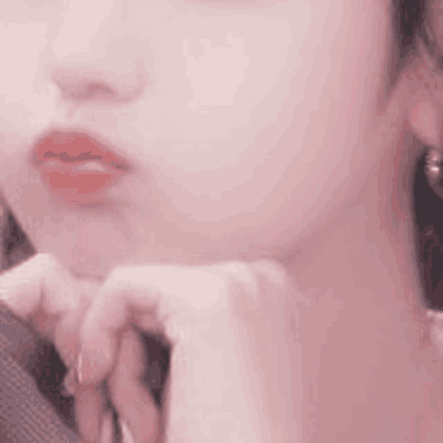 a close up of a woman 's face with her hand on her chin . she is wearing earrings .