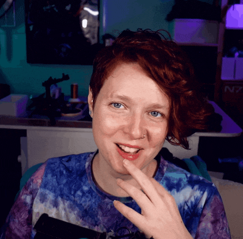 a woman with red hair and blue eyes is smiling in front of a desk that has the letter n7 on it
