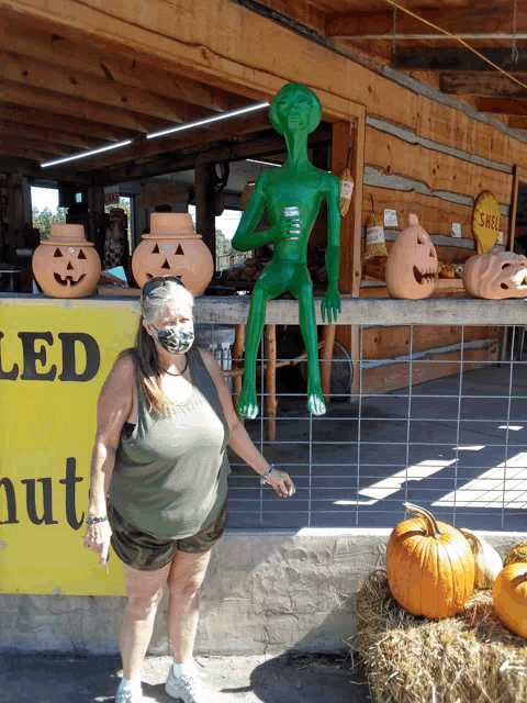 a woman wearing a mask stands in front of a green alien statue