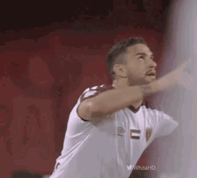 a soccer player in a white jersey with a red stripe on the sleeves throws a ball in the air .