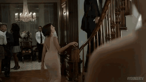 a woman in a white dress is dancing on the stairs while a man in a suit stands behind her .